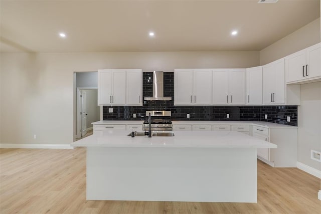 kitchen featuring a kitchen island with sink, wall chimney exhaust hood, stainless steel gas range, and light wood-style flooring