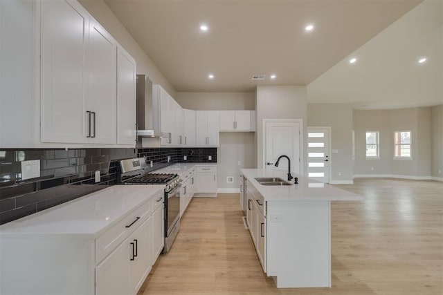 kitchen featuring stainless steel gas stove, light wood finished floors, tasteful backsplash, wall chimney exhaust hood, and a sink