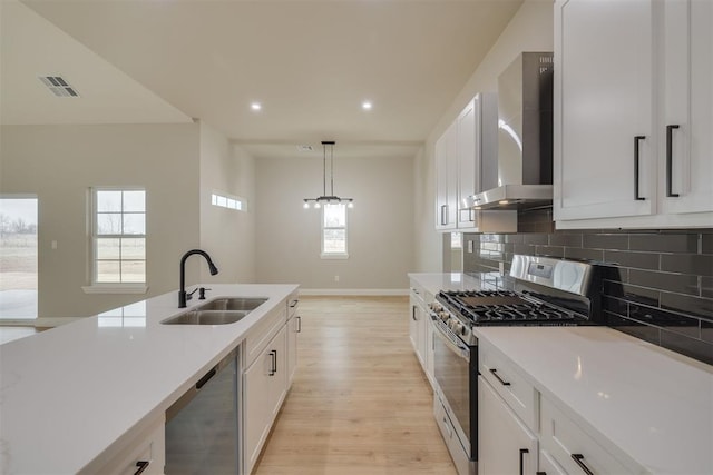 kitchen with visible vents, backsplash, appliances with stainless steel finishes, a sink, and wall chimney range hood