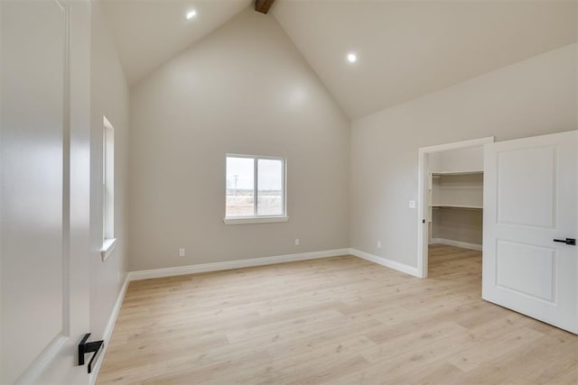 empty room with baseboards, high vaulted ceiling, and light wood-style floors