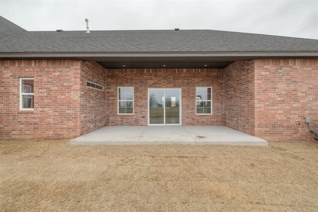 back of property featuring a patio area, brick siding, and roof with shingles