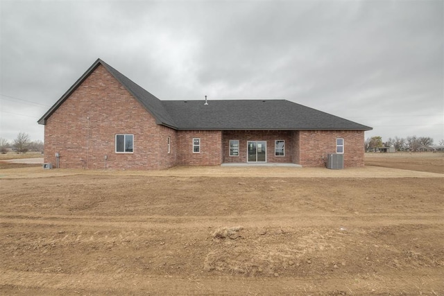 rear view of property with a shingled roof, a patio, cooling unit, and brick siding