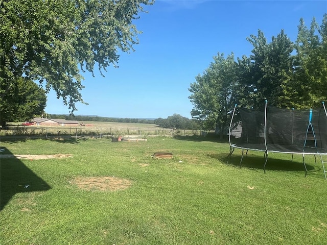 view of yard with a trampoline, a rural view, and fence