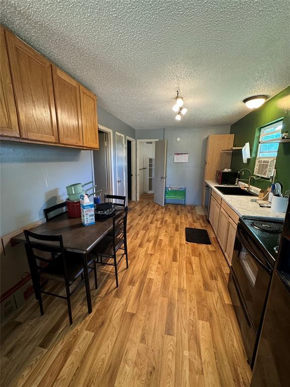 kitchen with light wood finished floors, black range with electric stovetop, brown cabinetry, and a sink