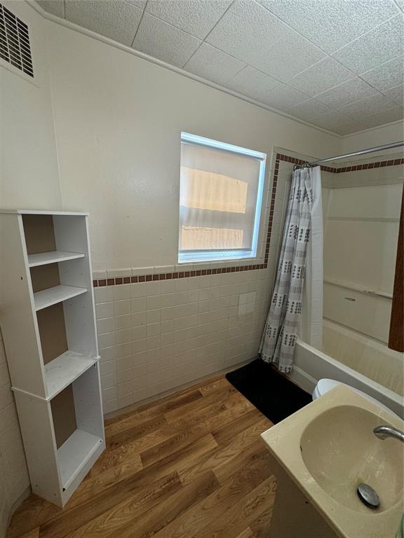 full bathroom with shower / bath combo, visible vents, tile walls, wood finished floors, and a sink