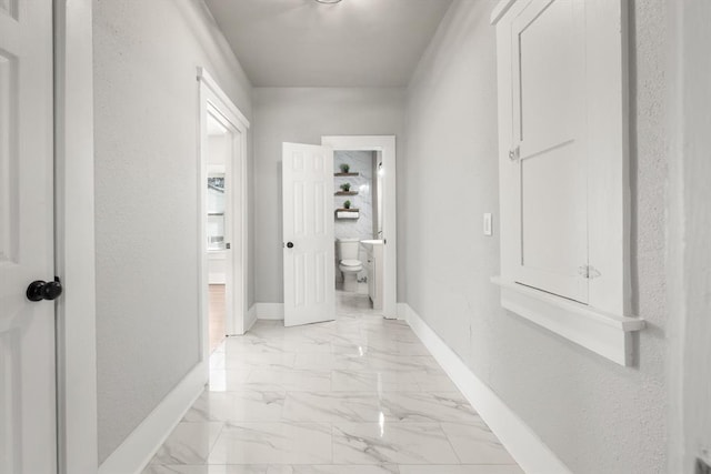 hall with a textured wall, marble finish floor, and baseboards