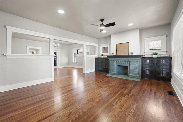 interior space with ceiling fan with notable chandelier, a fireplace, wood finished floors, visible vents, and baseboards