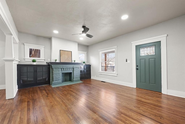 unfurnished living room featuring a fireplace with flush hearth, ceiling fan, wood finished floors, and baseboards