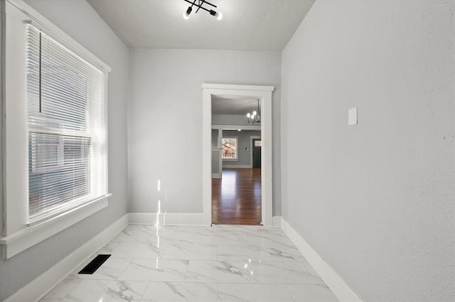 spare room with marble finish floor, an inviting chandelier, visible vents, and baseboards