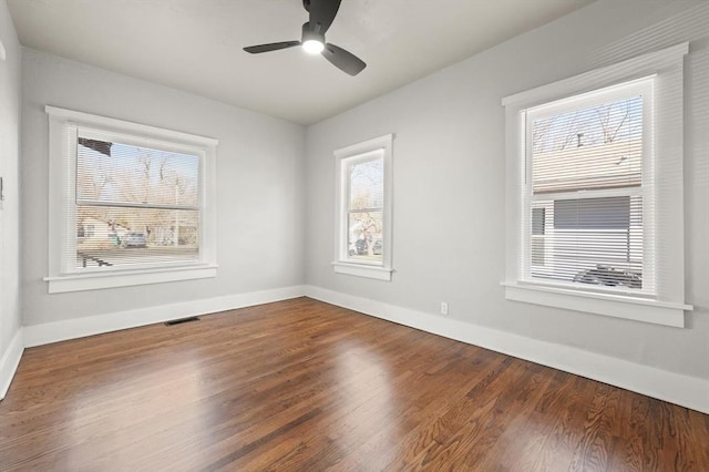 spare room with a ceiling fan, visible vents, baseboards, and wood finished floors