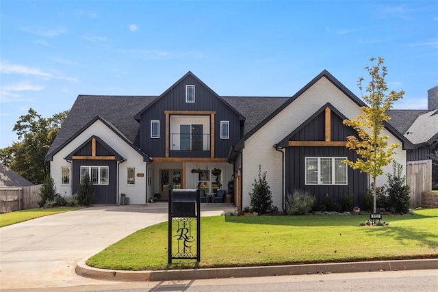 modern farmhouse style home featuring board and batten siding, a front yard, a shingled roof, and a balcony