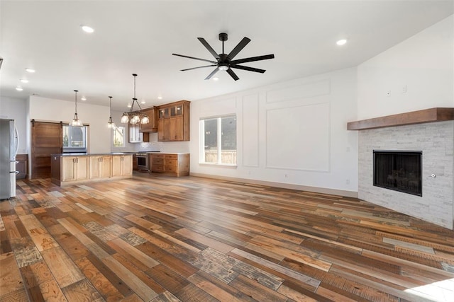 unfurnished living room featuring dark wood-style flooring, a fireplace, recessed lighting, a decorative wall, and a ceiling fan