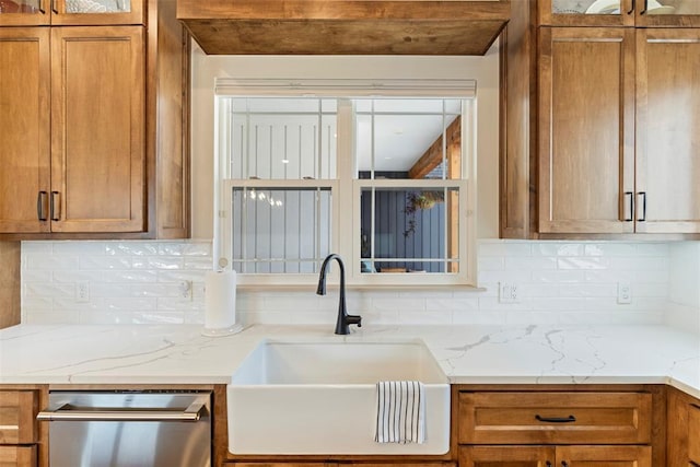 kitchen featuring dishwasher, glass insert cabinets, brown cabinets, a sink, and backsplash