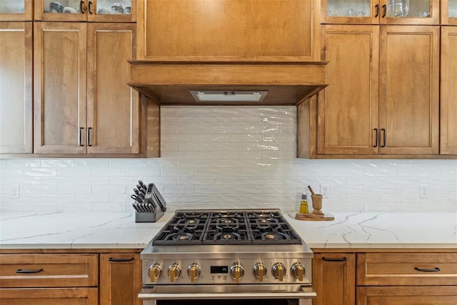 kitchen featuring high end stainless steel range oven, glass insert cabinets, brown cabinets, and decorative backsplash