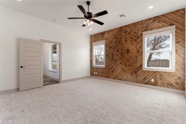 carpeted spare room featuring visible vents, ceiling fan, wooden walls, and baseboards