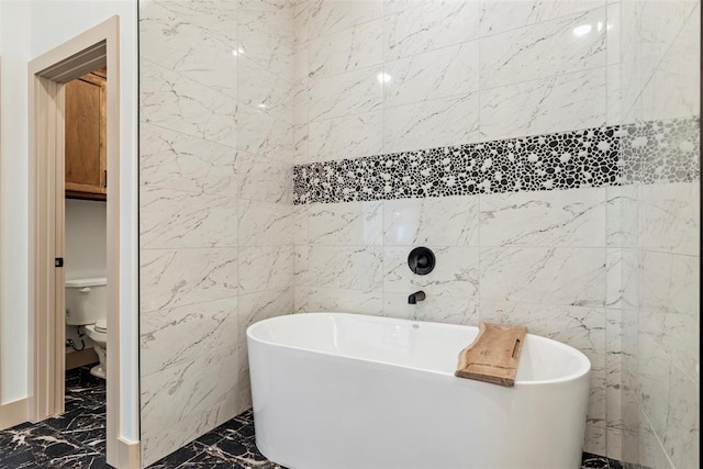 bathroom with toilet, marble finish floor, and a freestanding tub