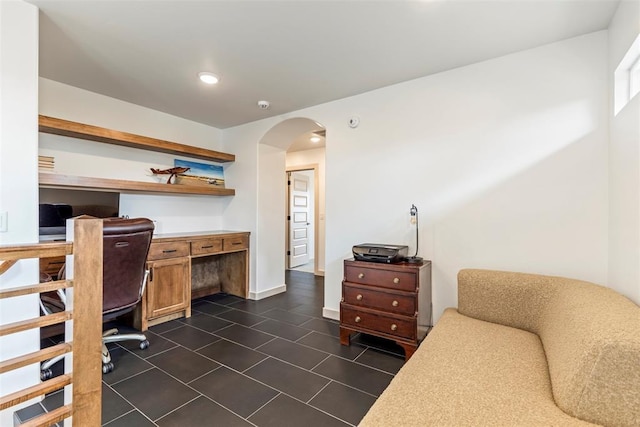 home office featuring arched walkways, built in desk, recessed lighting, dark tile patterned flooring, and baseboards