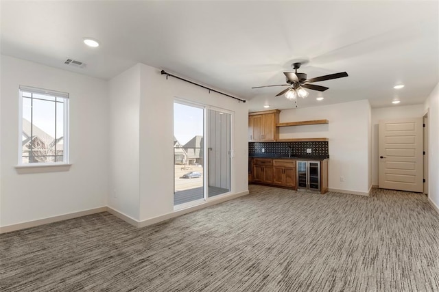 unfurnished living room featuring beverage cooler, visible vents, baseboards, and a healthy amount of sunlight