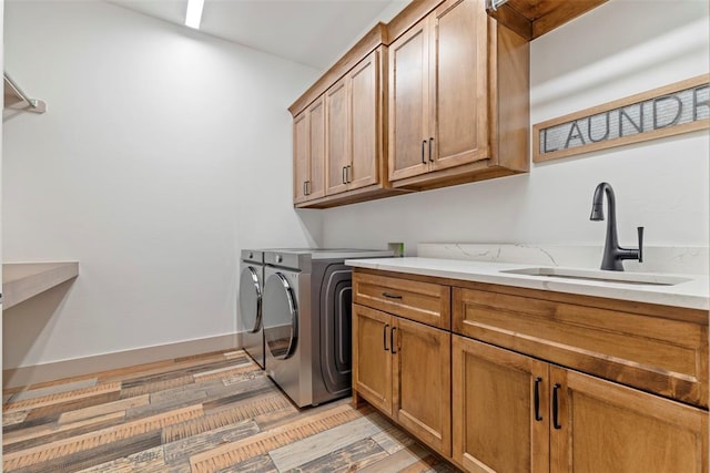 clothes washing area with washer and dryer, cabinet space, a sink, light wood-type flooring, and baseboards