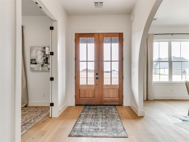 doorway featuring arched walkways, visible vents, baseboards, french doors, and light wood finished floors