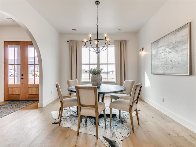 dining room with arched walkways, light wood-style flooring, a notable chandelier, baseboards, and french doors