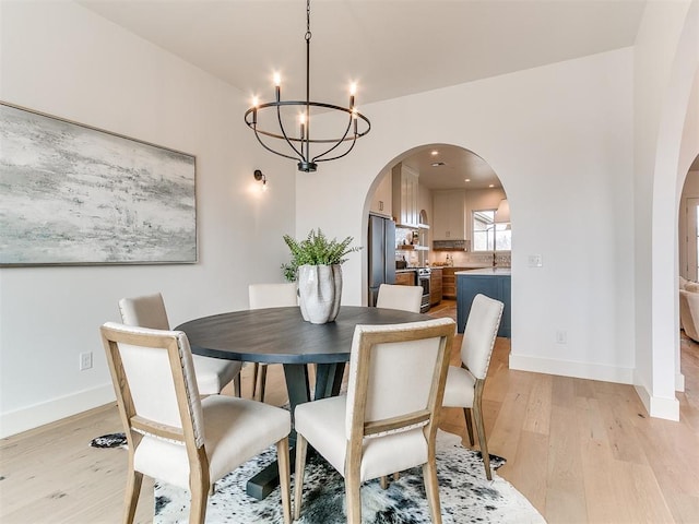 dining area featuring arched walkways, an inviting chandelier, baseboards, and light wood-style floors