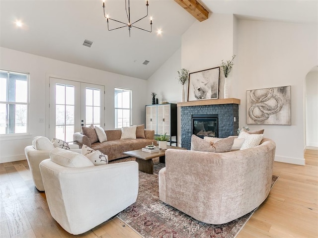 living area featuring light wood-style floors, a glass covered fireplace, a wealth of natural light, and beamed ceiling