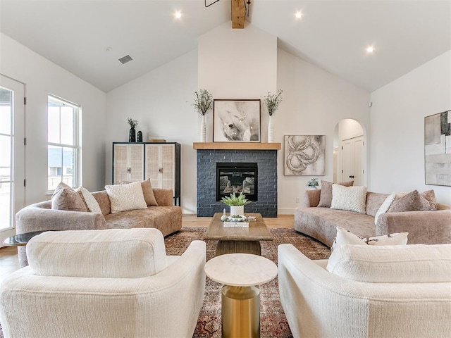 living room featuring visible vents, arched walkways, a glass covered fireplace, wood finished floors, and beamed ceiling