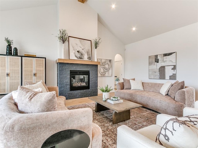 living area featuring arched walkways, high vaulted ceiling, a fireplace, and wood finished floors