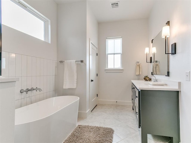 full bathroom featuring visible vents, a freestanding bath, vanity, baseboards, and tile patterned floors