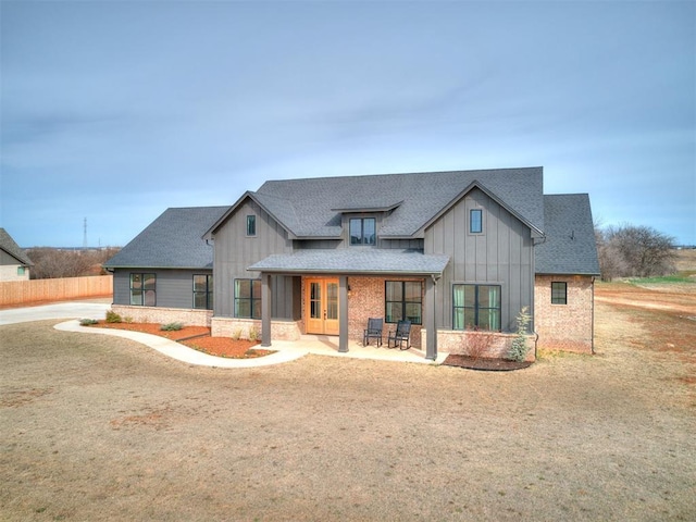 modern inspired farmhouse with stone siding, board and batten siding, a patio area, and roof with shingles