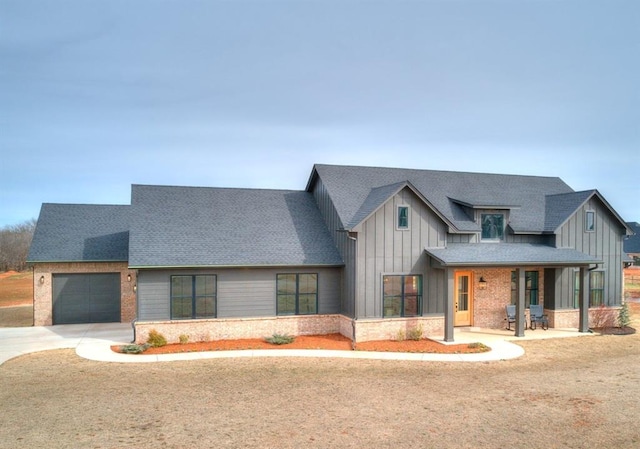 modern farmhouse featuring driveway, roof with shingles, an attached garage, board and batten siding, and brick siding