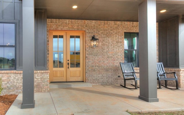 doorway to property with covered porch, french doors, and brick siding