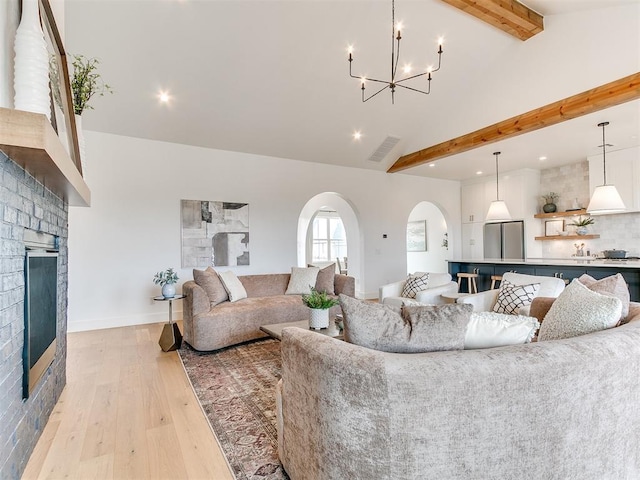 living room featuring arched walkways, beam ceiling, a fireplace, visible vents, and light wood-style floors