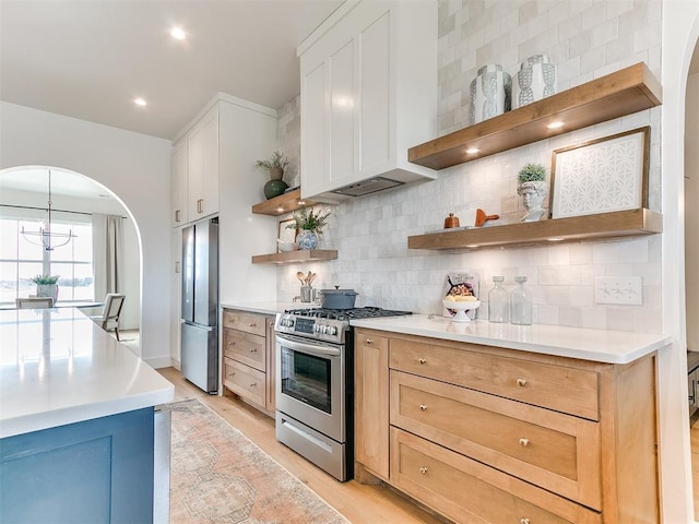 kitchen with arched walkways, stainless steel appliances, light countertops, decorative backsplash, and open shelves