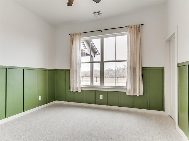 spare room featuring carpet floors, visible vents, ceiling fan, and a decorative wall