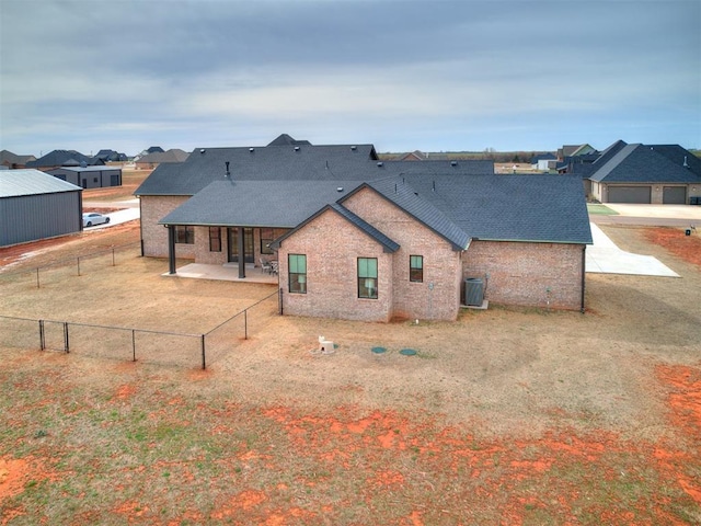 rear view of property with brick siding, a fenced backyard, a shingled roof, and a patio