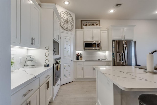 kitchen with stainless steel appliances, light wood-type flooring, white cabinets, and visible vents