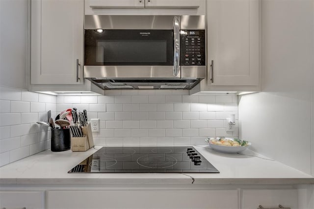 kitchen with black electric cooktop, white cabinetry, light countertops, backsplash, and stainless steel microwave