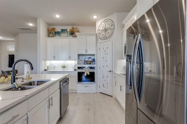 kitchen featuring stainless steel appliances, light countertops, light wood-style flooring, white cabinets, and a sink