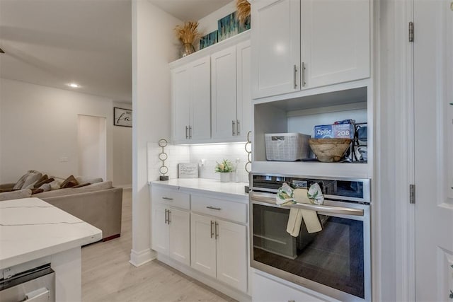 kitchen featuring decorative backsplash, light stone counters, stainless steel oven, light wood-style floors, and white cabinetry