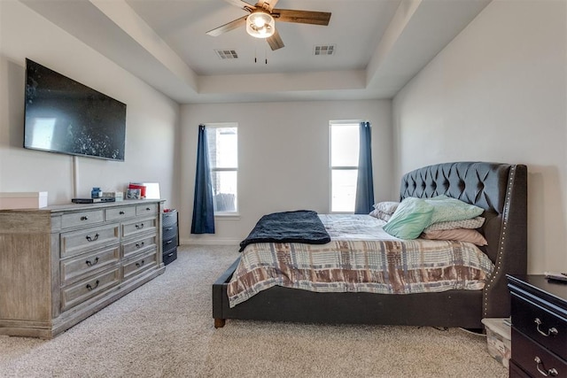 bedroom featuring carpet floors, a tray ceiling, visible vents, and a ceiling fan