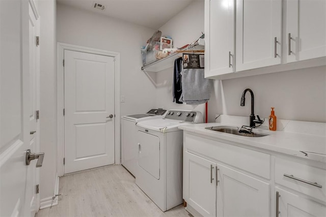 clothes washing area featuring cabinet space, visible vents, independent washer and dryer, light wood-style floors, and a sink