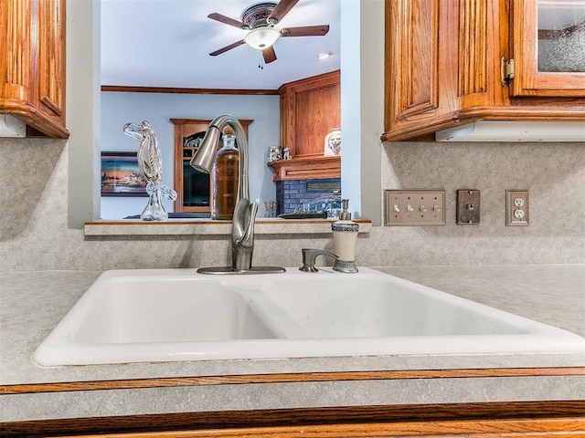 interior details featuring brown cabinetry, ceiling fan, light countertops, crown molding, and a sink