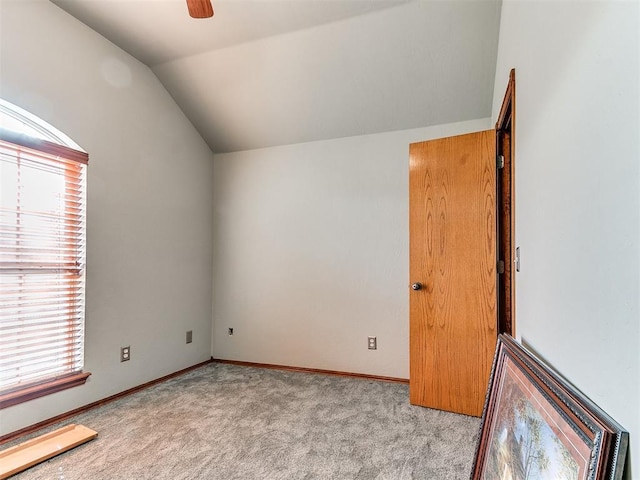 empty room featuring lofted ceiling, baseboards, a ceiling fan, and light colored carpet