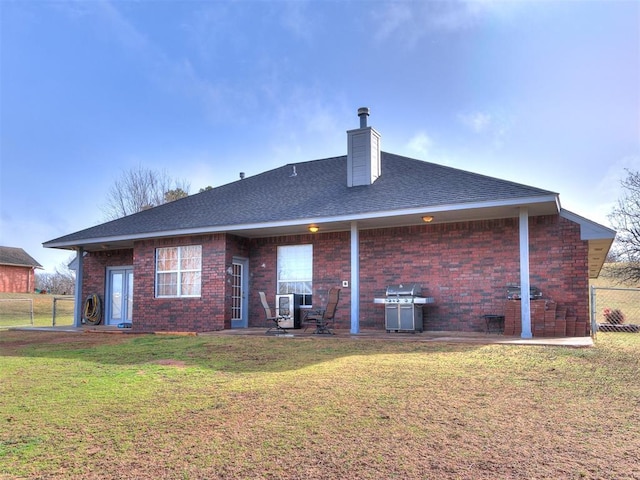 rear view of house with roof with shingles, brick siding, a yard, and fence