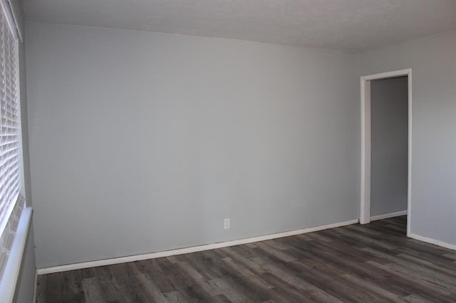 spare room featuring baseboards and dark wood-type flooring