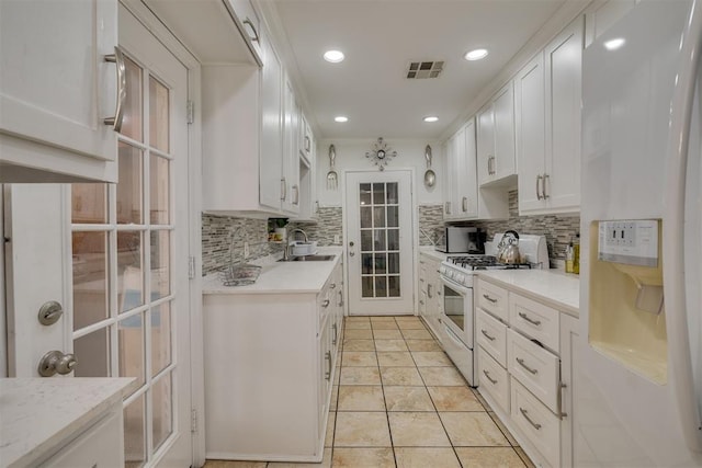 kitchen featuring light countertops, backsplash, white cabinetry, a sink, and white appliances