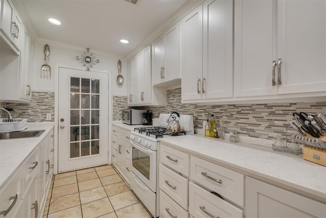 kitchen featuring light tile patterned floors, white range with gas stovetop, a sink, white cabinets, and decorative backsplash