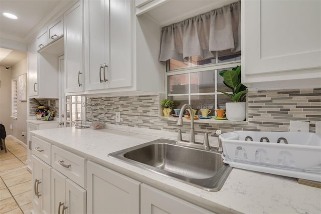 kitchen with light tile patterned floors, light stone counters, white cabinetry, tasteful backsplash, and crown molding